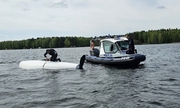 policjant na łodzi policyjnej, a drugi policjant podczas udzielania pomocy sternikowi na przewróconej żaglówce
