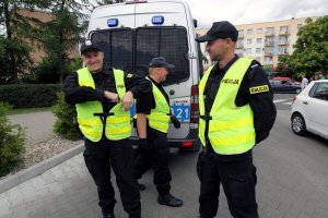 trzej uśmiechęci policjanci stoją obok radiowozu