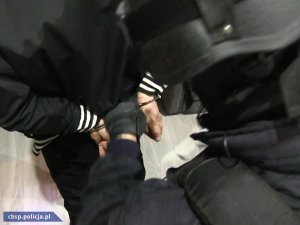 Policjant zakłada kajdanki jednemu z zatrzymanych