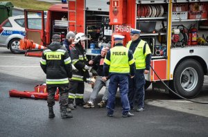 policjanci i strażacy przy wozie strażackim udzielają pomocy rannemu