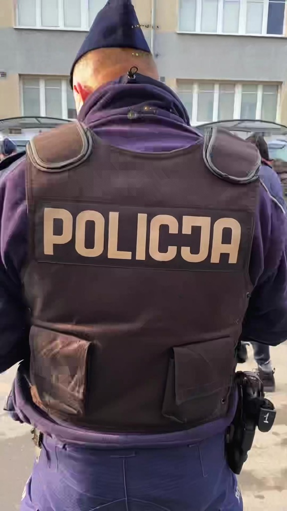 Policjant w kamizelce z napisem POLICJA na plecach.