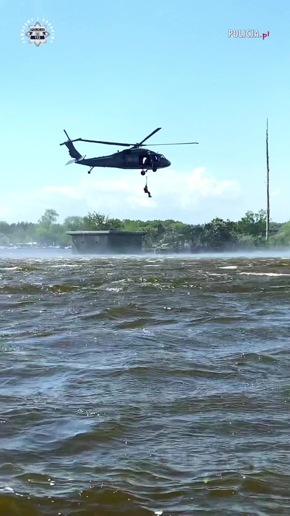 Helikopter nad taflą wody, pod nim człowiek zwisający na linie.