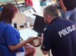 Umundurowany policjant z pielęgniarką w niebieskim kitlu siedzą przy laptopie i piszą tekst na klawiaturze komputera