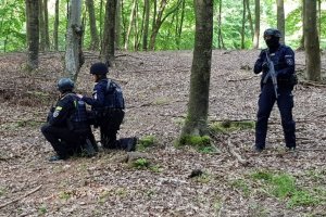 Policjanci w lesie z bronią długą.