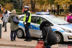 policjant przy radiowozie oraz mieszkańcy Warszawy