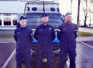 trzej policjanci stoją przed radiowozem