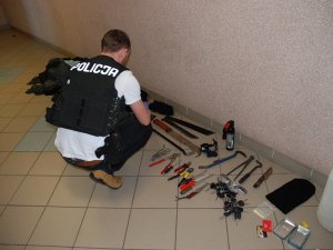 policjant ogląda zabezpieczone przedmioty leżące pod ścianą na podłodze
