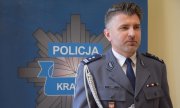 Komendant Miejski Policji w Krakowie mł. insp. Zbigniew Nowak stoi na tle ściany z logiem Policji z Krakowa