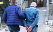Nieumundurowany policjant prowadzi podejrzanego mężczyznę do Komisariatu Policji Warszawa Ursynów. Mężczyzna ma kajdanki założone na ręce z tyłu