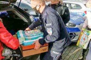 umundurowany policjant wyjmuje rzeczy dla dzieci z bagażnika samochodu, w tle pomagają mu kobiety