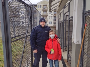 umundurowany policjant stoi z chłopcem na zewnątrz przed budynkiem Komendy Powiatowej