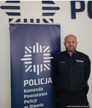 Umundurowany policjant na tle banera z napisem Komenda Powiatowa Policji w Brzegu