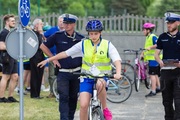 jeden z zawodników turnieju jedzie na rowerze, z tyłu widać dwóch umundurowanych policjantów