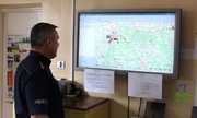Dyżurny jednostki Policji patrzy na wiszący przed nim na ścianie ekran, na którym wyświetla się mapa