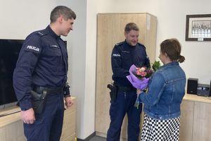 Zdjęcie przedstawia umundurowanych policjantów, którzy stoją w jednym pomieszczeniu. Przed jednym z nich stoi kobieta i trzyma w dłoniach kolorowy bukiet kwiatów.