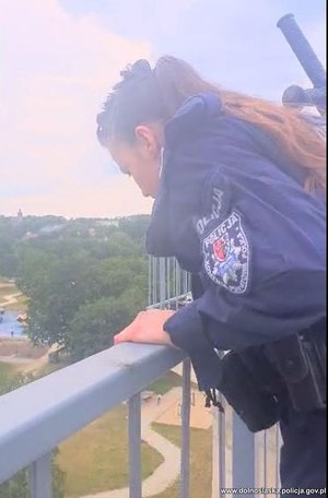 Na zdjęciu policjantka pochylająca się na moście i patrząca w dół