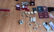 na stole leżą odzyskane przez policjantów przedmioty skradzione przez mężczyznę: dwa paszporty, monety kolekcjonerskie, dwie karty pojazdu, plik banknotów i bizuteria