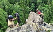 Dwaj policjanci Samodzielnego pododdziału kontrterrorystycznego Policji we Wrocławiu wraz z ratownikiem Górskiego Ochotniczego Pogotowia Ratunkowego przygotowują się do wspinaczki po skałach, w tle las