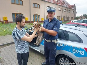 Policjant stojący przy radiowozie przekazuje psa właścicielowi