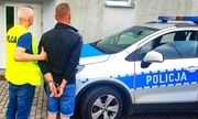 umundurowany policjant prowadzi zatrzymanego mężczyznę, w tle radiowóz policyjny