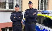 dwóch umundurowanych policjantów stojących przy radiowozie. W tle Komisariat Policji III w Sosnowcu