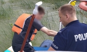 Policjant na policyjnej łodzi pomaga mężczyźnie nadesce SUP wejść na łódź
