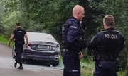 trzech policjantów na drodze w tle stoi samochód
