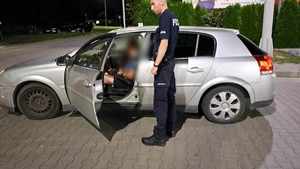 Umundurowany policjant stoi przy otwartych drzwiach auta, w którym siedzi kierowca