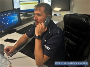 Siedzący przy biurku, ze słuchawką w dłoni umundurowany policjant