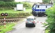 Samochód na przejeździe kolejowym z opuszczonymi rogatkami i przejeżdżający pociąg