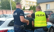dwaj policjanci z zatrzymanym mężczyzną przy radiowozie policyjnym