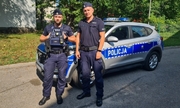 Zdjęcie dwóch policjantów, którzy stoją obok oznakowanego radiowozu