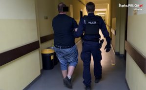 Policjant prowadzi korytarzem zatrzymanego mężczyznę