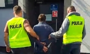 dwaj policjanci prowadzą zatrzymanego mężczyznę zakutego w kajdanki