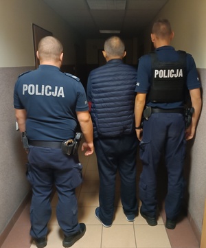 dwaj umundurowani policjanci prowadzą korytarzem zatrzymanego mężczyznę