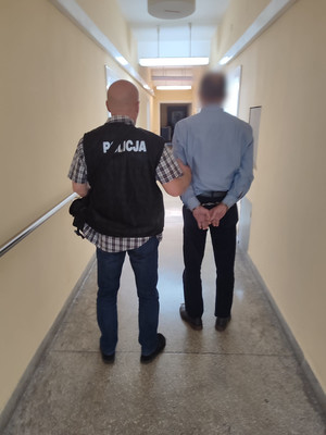 policjant prowadzi korytarzem zatrzymanego mężczyznę zakutego w kajdanki