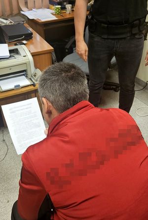 Zatrzymany mężczyzna siedzi i czyta dokumenty. Obok stoi policjant