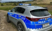 radiowóz policyjny stoi na polnej drodze, w tle wzniesienia