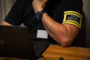 Policjant pracuje na laptopie, na ramieniu ma opaskę CBZC Policja.