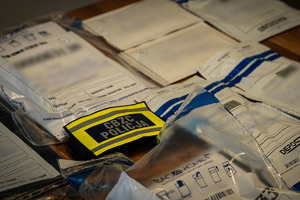 Zabezpieczone przedmioty w foliowych workach, pomiędzy nimi opaska z napisem CBZC Policja.
