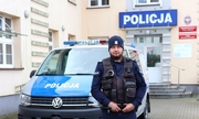 policjant stoi przed radiowozem policyjnym, w tle budynek komendy Policji w Bytowie