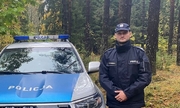 policjant stoi przy radiowozie na drode leśnej