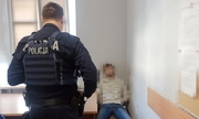 Mężczyzna siedzi przy biurku a obok stoi umundurowany policjant