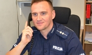 umundurowany policjant siedzi przy biurku, w ręku trzyma słuchawkę telefonu
