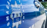 Odznaka policyjna na drzwiach radiowozu z napisem pomagamy i chronimy oraz policja i numerem alarmowym 112