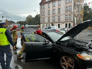 policjant i strażacy podczas gaszenia palącego się samochodu