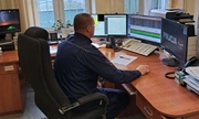 Dyżurny siedzi przy swoim stanowisku służby. Na biurku, przy którym siedzi znajdują się trzy monitory komputerowe oraz telefon.