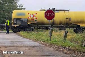 Znak STOP przed widocznym przejazdem kolejowym, na którym stoi wagon-cysterna