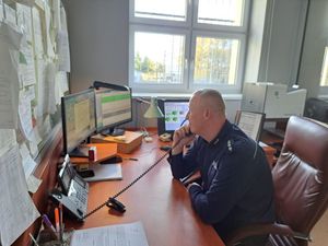 policjant siedzi przy biurku rozmawiając przez telefon, w tle okno