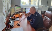 policjant siedzi przy biurku rozmawiając przez telefon, w tle okno